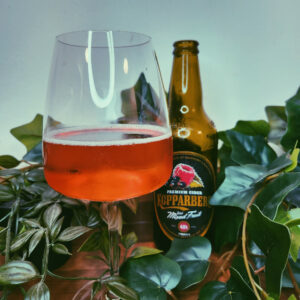 kopparberg mixed fruit in a glass with the cider bottle behind, wrapped in leaves