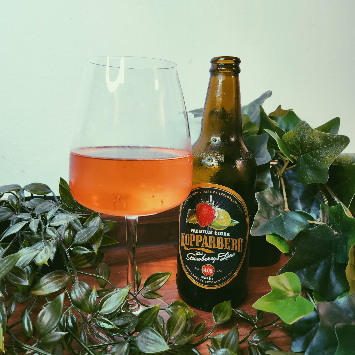 kopparberg strawberry and lime fruit cider bottle next to a wine glass filled with the strawberry pink cider.
