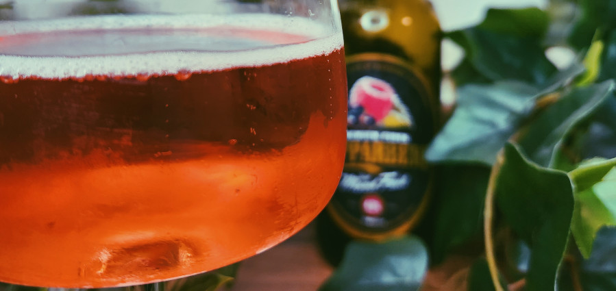 close up of kopparberg mixed fruit cider in a wine glass with the bottle blurred in the background