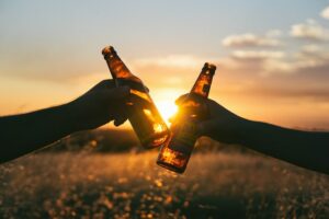 two people doing a cheers action with cider bottles infront of the setting sun.