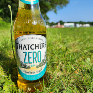 A bottle of Thatchers zero in a field on a sunny day.